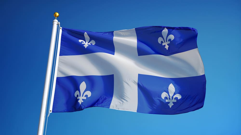 Quebec flag waving against clean blue sky, close up, isolated with clipping path mask alpha channel transparency. Source: Shutterstock.com