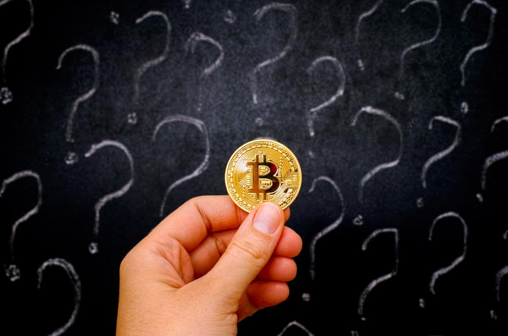 Woman hand with golden Bitcoin virtual money against blackboard with question marks. Source: Shutterstock.com