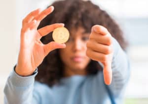 African american woman holding golden bitcoin cryptocurrency at home with angry face, negative sign showing dislike with thumbs down, rejection concept Source; shutterstock.com