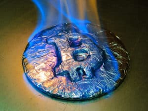 Bitcoin metal silver coin is burning with blue flame. It means hot price or value and high exchange rate of crypto currency on market. It is crisis and fall to lose investments due to financial risk. Source: shutterstock.com