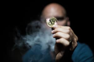 bald man holds a bitcoin in a smoky dark place. - Image