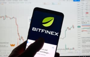 MONTREAL, CANADA - APRIL 26, 2019 Bitfinex cryptocurrency exchange logo and application on Android Samsung Galaxy s9 Plus screen in a hand over a laptop display with bitcoin chart on it. - Image